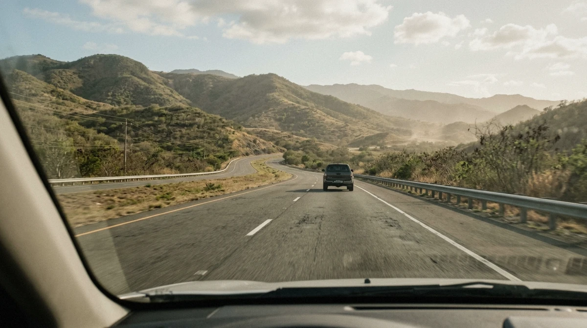 Open highway cutting through dry green hills on the south coast of Puerto Rico in late afternoon